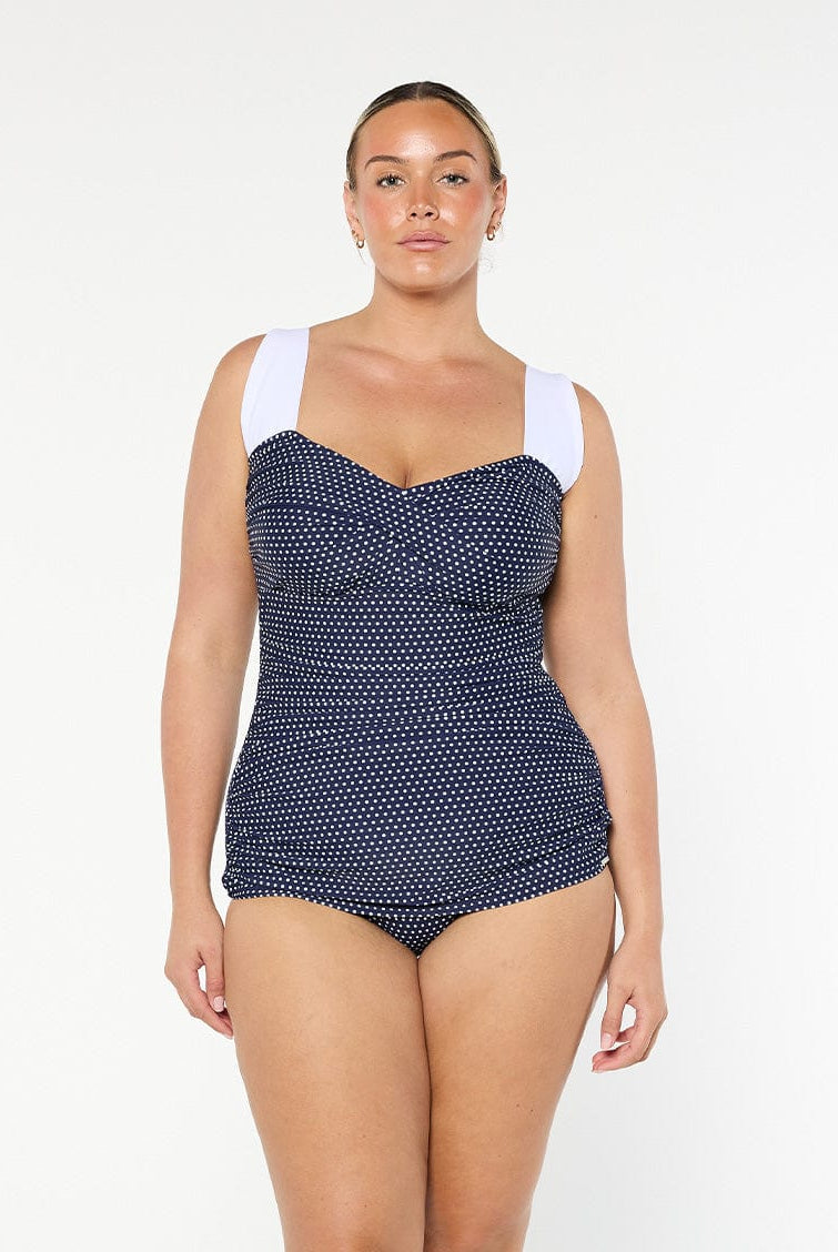 Woman wearing a navy polka dot swimsuit with white straps on a white background