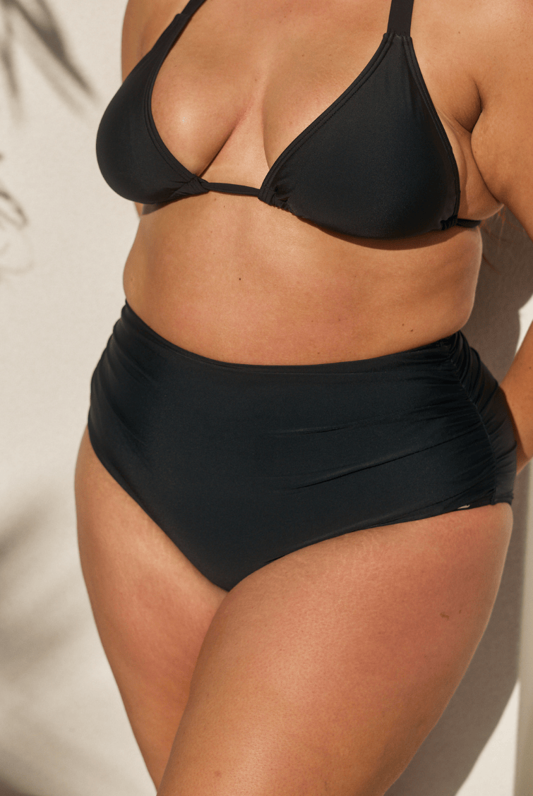 Person wearing black high-waisted bikini bottoms on a plain background