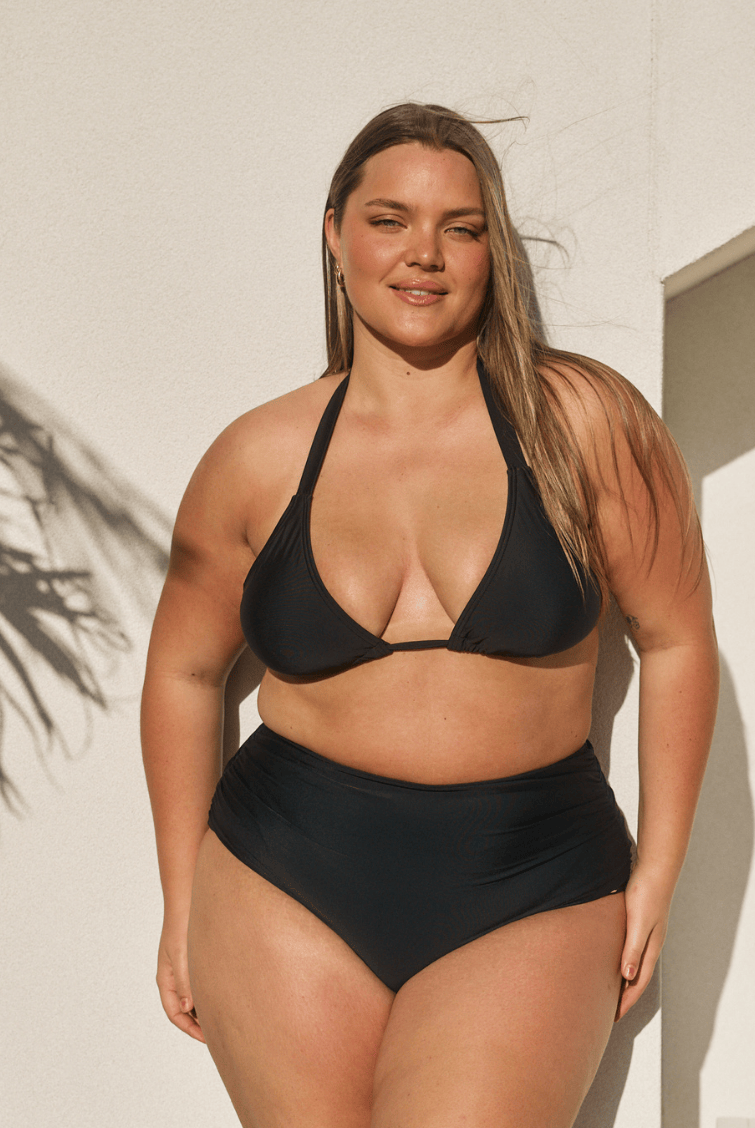 Person wearing black high-waisted bikini bottoms on a plain background