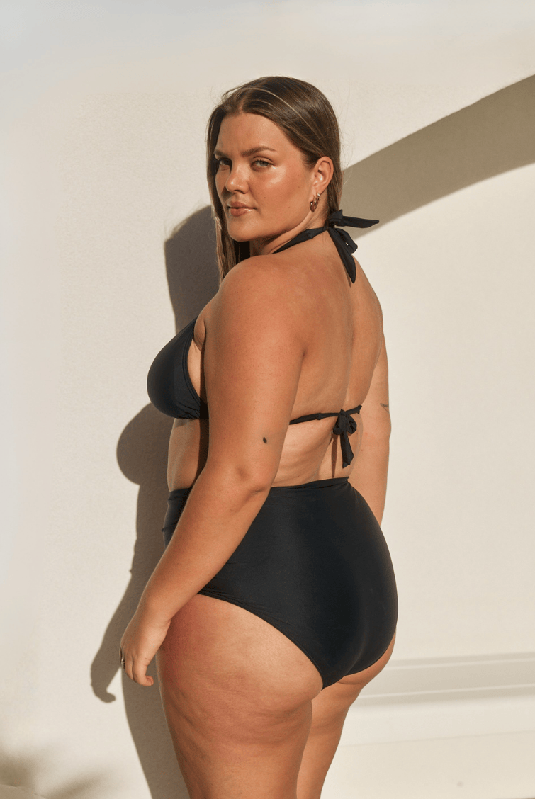 Person wearing black high-waisted bikini bottoms on a plain background