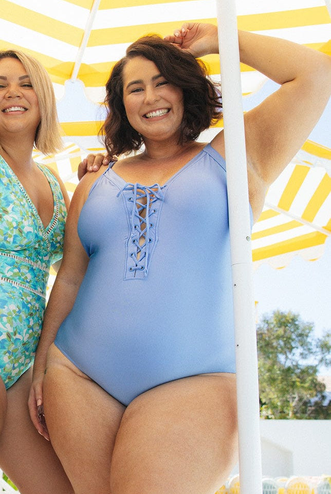 brunette model wearing lace up one piece in a light metallic blue