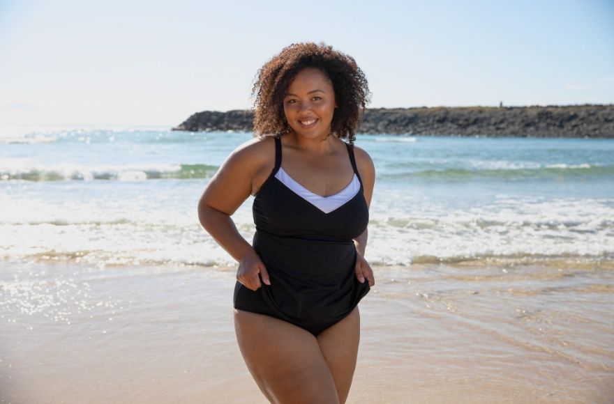 brunette woman poses on the beach wearing Acapulco black and white underwire tankini top with black high waisted pants