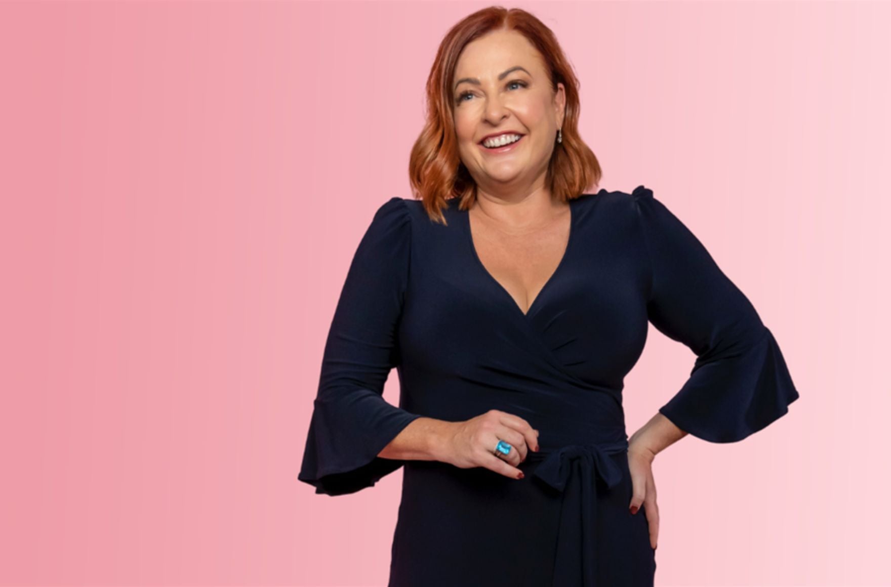 Shelly Horton wears v neck navy dress. Her hair is red and styled in a bob. She is smiling. 