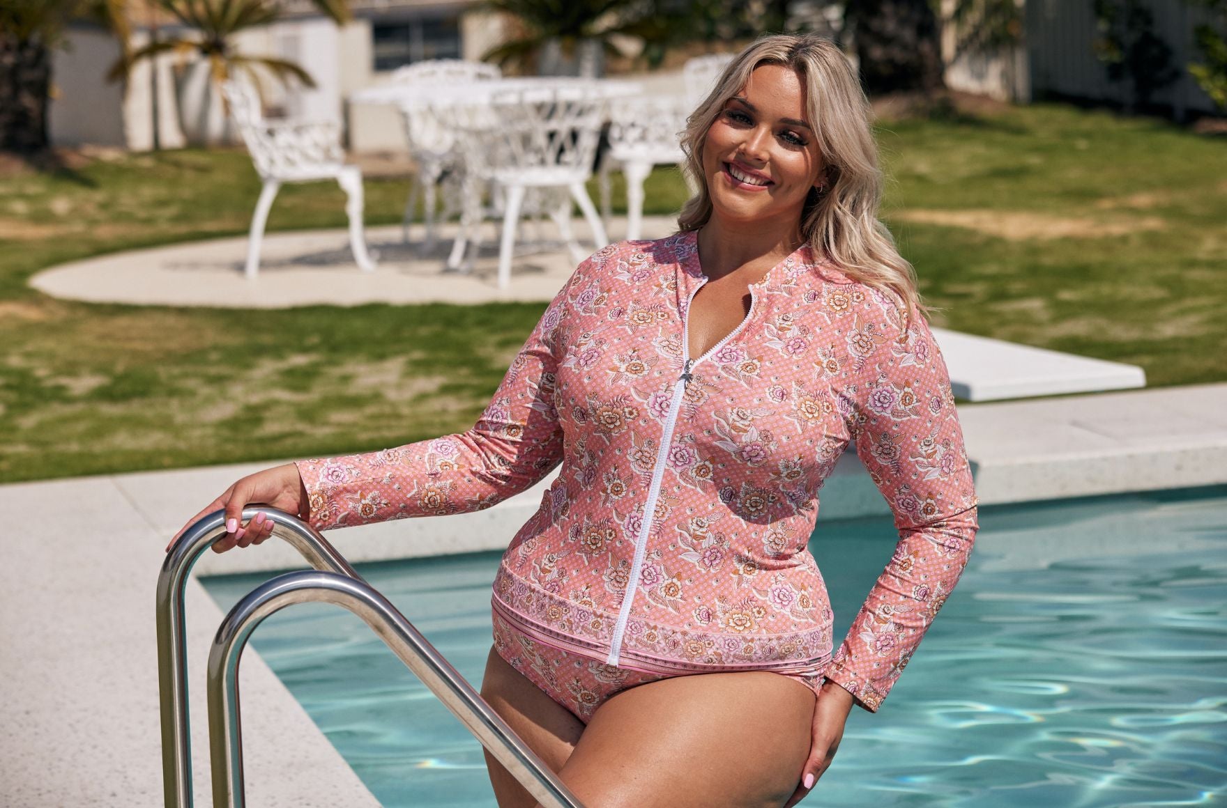 woman with blonde hair steps out of the pool wearing pink floral long sleeve rash vest and matching bikini bottoms