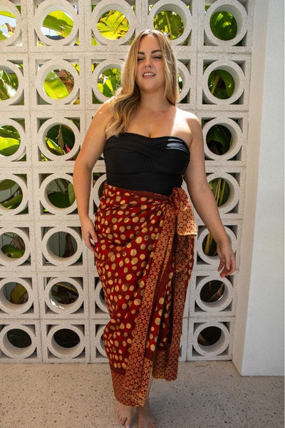 Maroon block printed spot design sarong worn over a black strapless swimsuit
