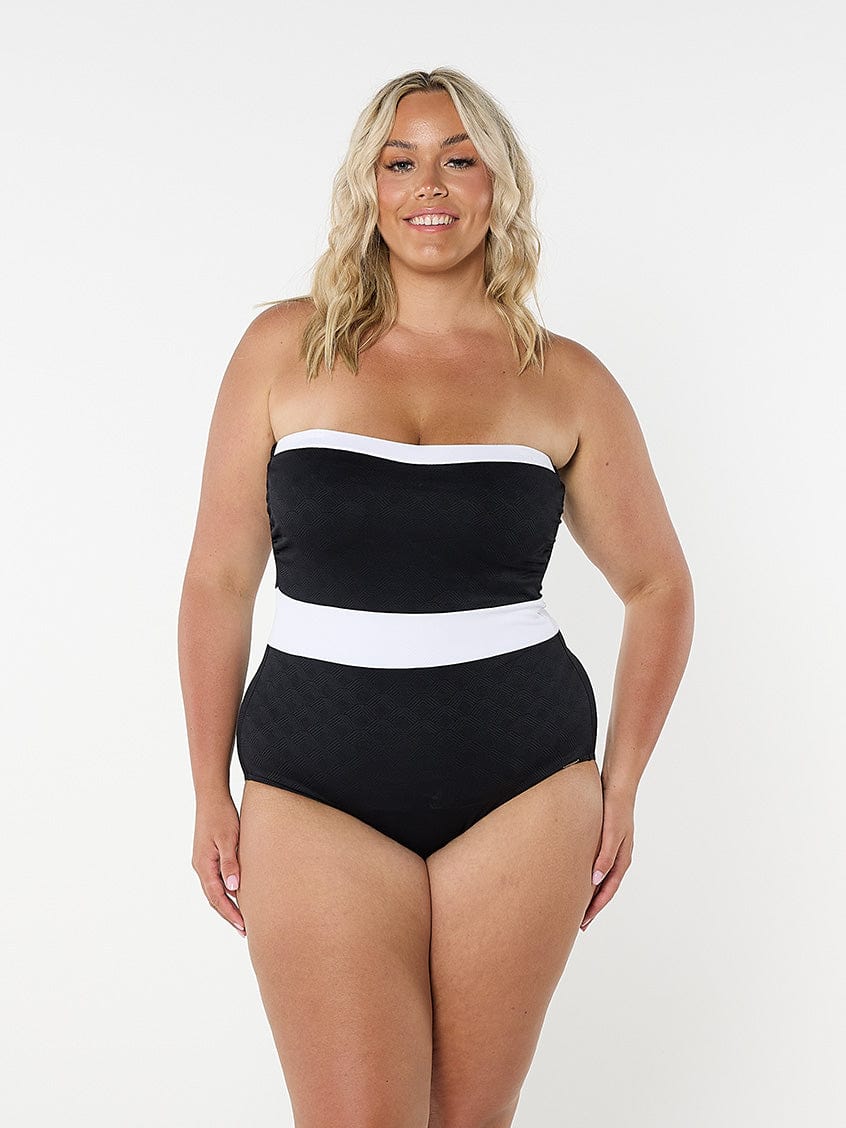 Woman wearing a black and white strapless swimsuit on a plain background