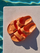 Pair of orange sandals on a diving board with water in the background