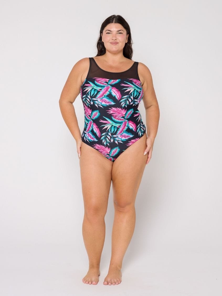 Woman wearing a black swimsuit with pink and green leaf pattern on a white background