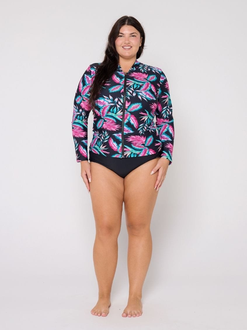 Woman wearing a colorful tropical leaf patterned rash guard on a white background
