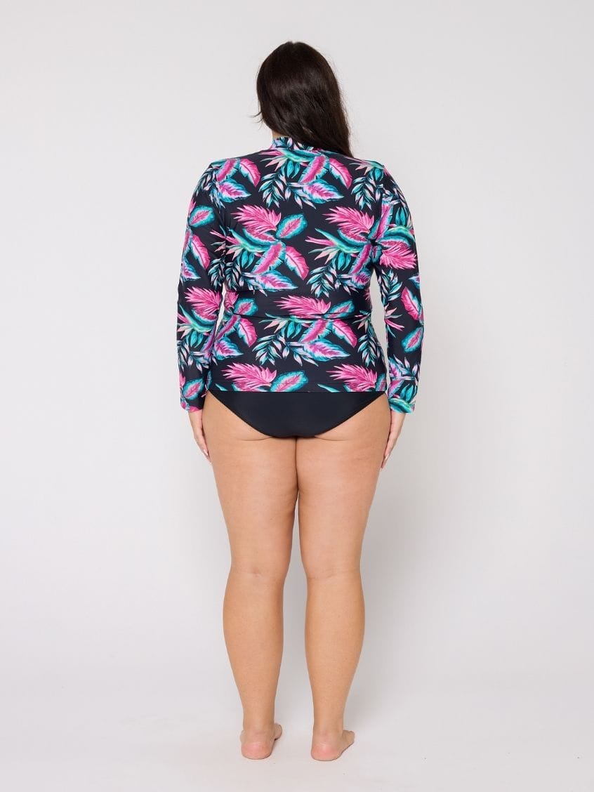 Woman wearing a colorful tropical print shirt over a swimsuit on a white background
