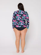 Woman wearing a colorful tropical print shirt over a swimsuit on a white background
