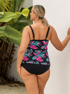 Woman wearing a black swimsuit with colorful floral pattern against a white wall.