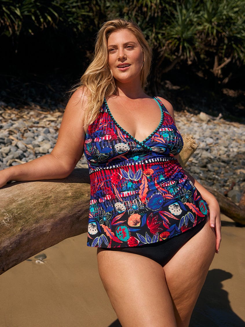 Blonde curve model posing on beach wearing a tankini top with v neckline and embroidered trim