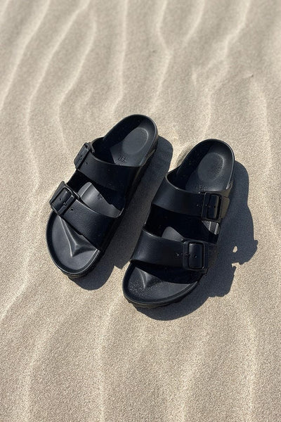 Black slip on sandals sitting on the beach for plus size women
