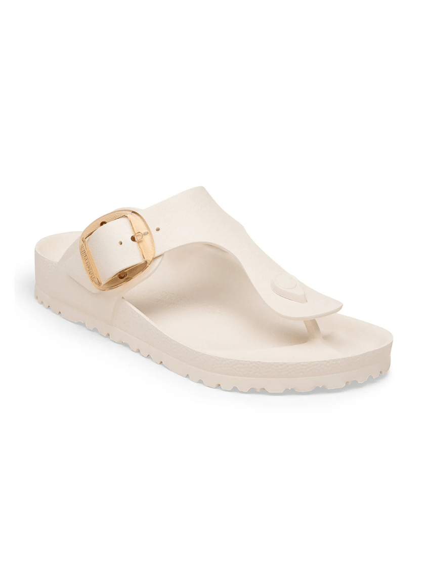 A single cream-colored thong sandal with a wide strap and a gold-tone buckle, shown from a side angle on a white background.
