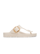 A single cream-colored thong sandal with a wide strap and a prominent gold buckle, shown in profile against a solid white background.