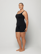 Woman wearing a black boyleg swimsuit against a white background