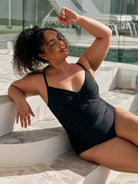 Brunette model wearing a black criss cross one piece for plus size women in black metallic fabric
