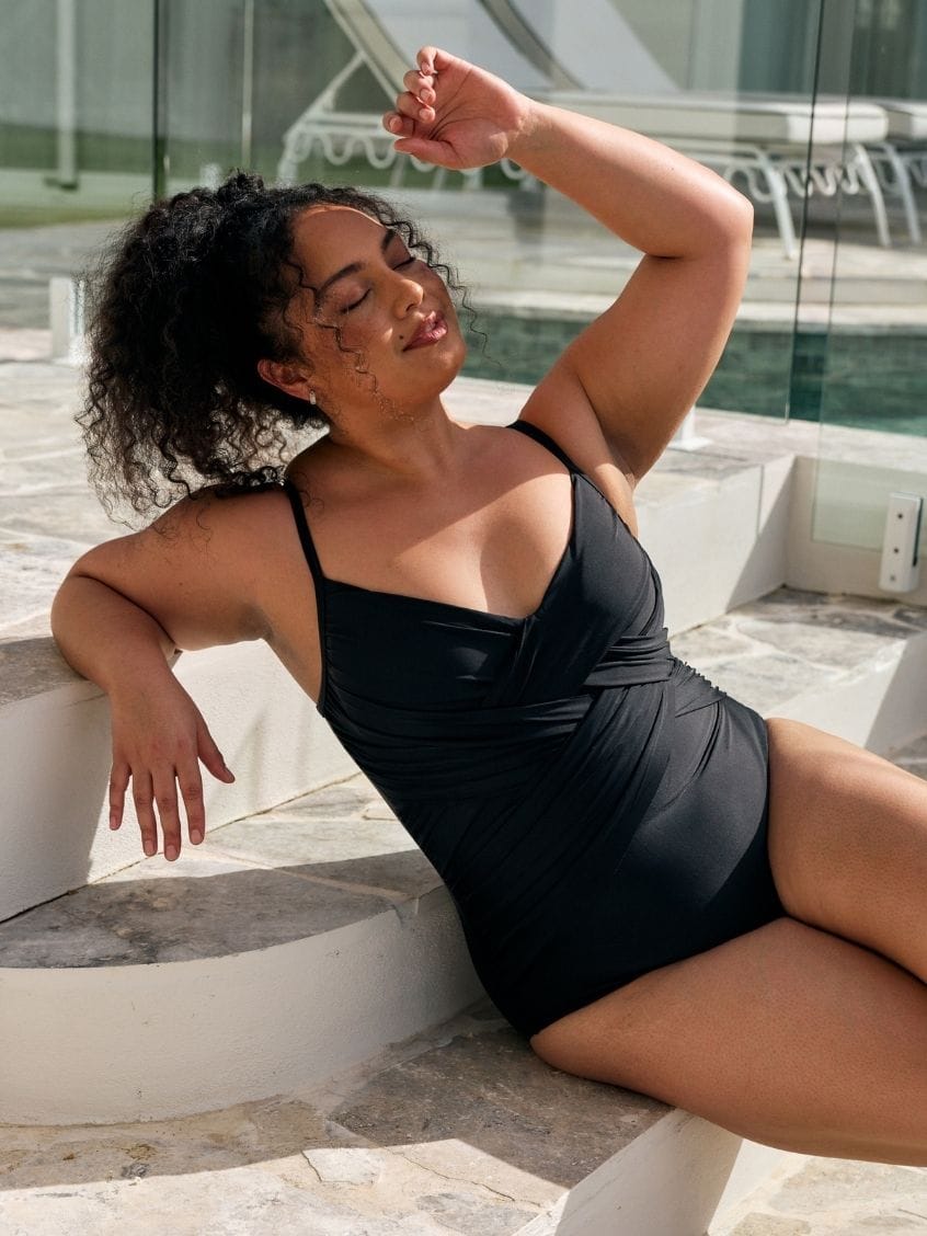Brunette model wearing a black criss cross one piece for plus size women in black metallic fabric
