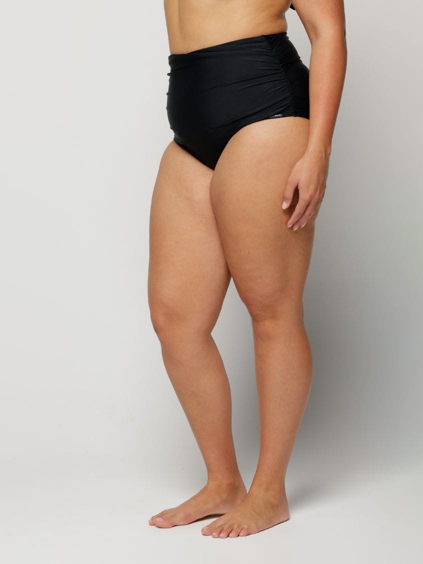 Person wearing black high-waisted bikini bottoms on a plain background