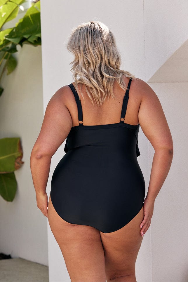 Blonde model showing back of black ruffle one piece with full coverage