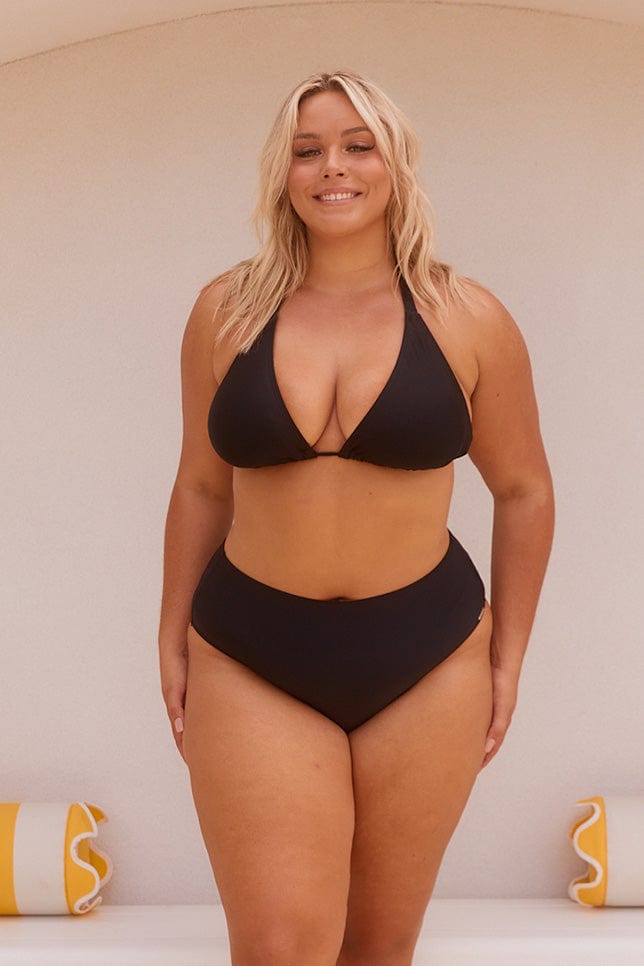 Blonde model wearing black bikini top and high waisted bottoms