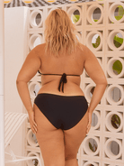 Person wearing a black bikini standing against a decorative stone wall.