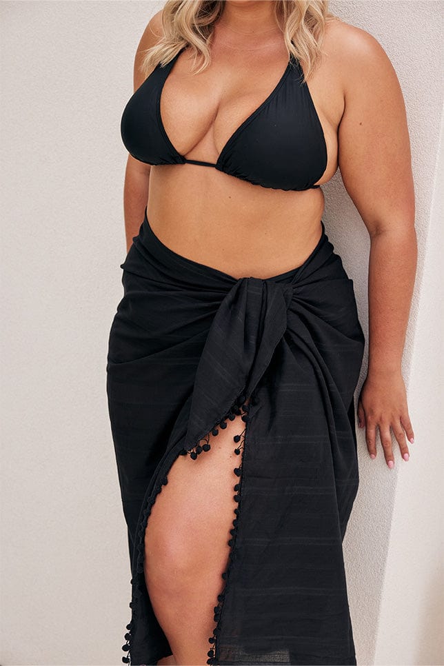 Close up of model wearing tied black sarong with pom poms