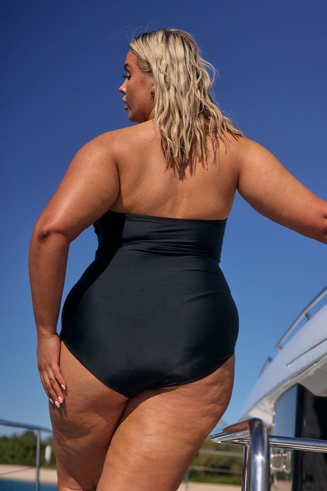 Blonde model showing back of black strapless womens one piece swimsuit