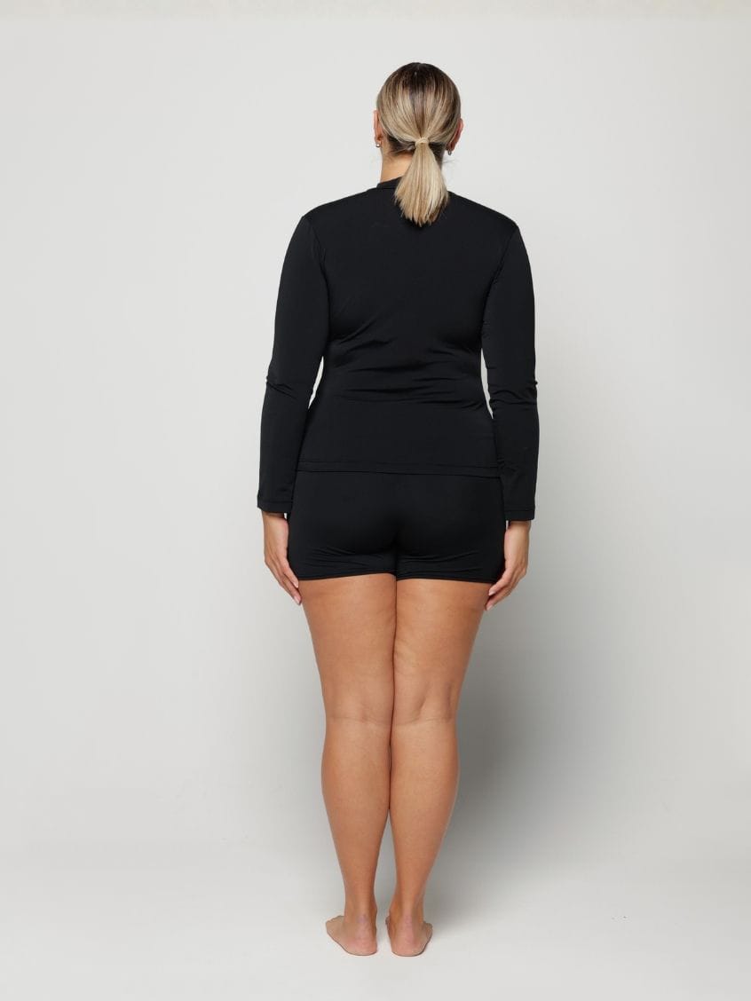 Woman wearing a black long-sleeve rash vest top with a zip and white background behind her