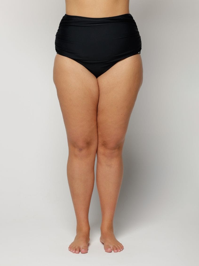 Woman wearing black high-waisted bikini bottoms on a plain background
