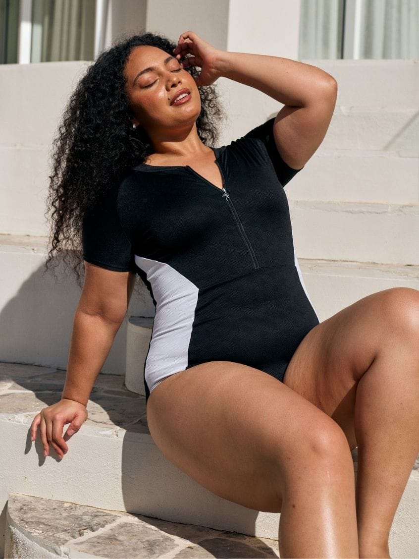 Close up image of model wearing a zip front detail one piece in black and white textured print