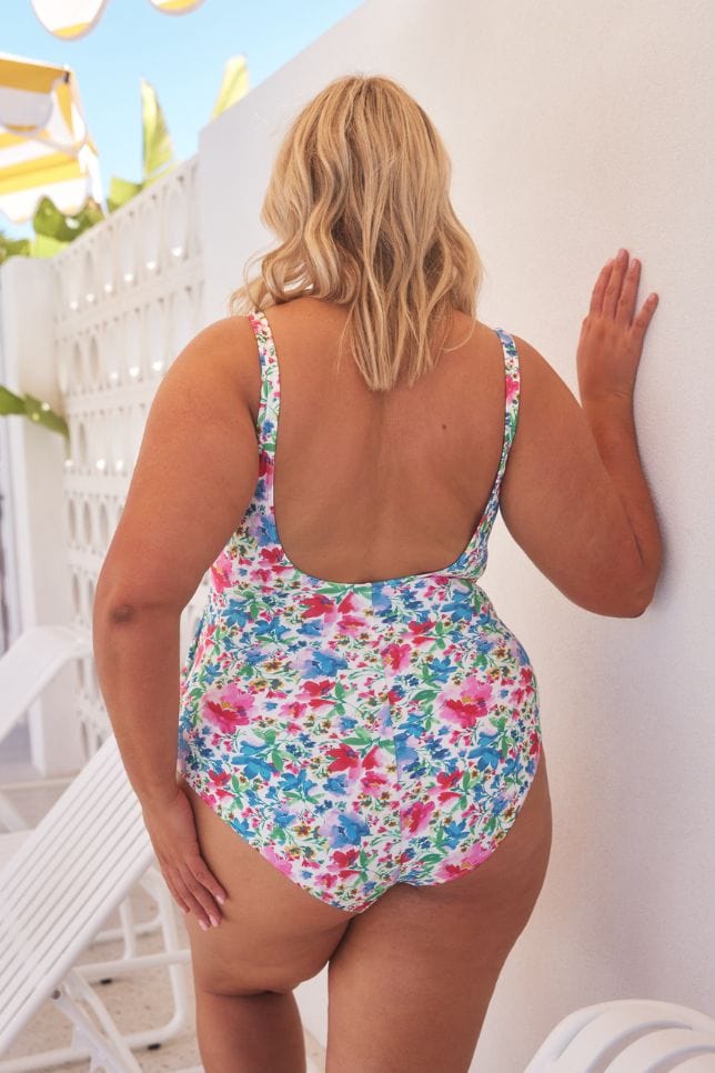 Back of model next to pool wearing scoop back one piece in bright floral coloured print with a crossover tie detail