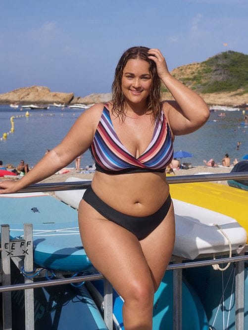 Woman in a striped bikini standing by boats on a sunny day