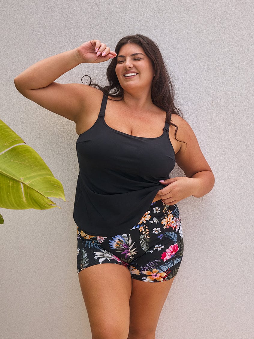 Woman wearing a black tank top and floral shorts against a plain background