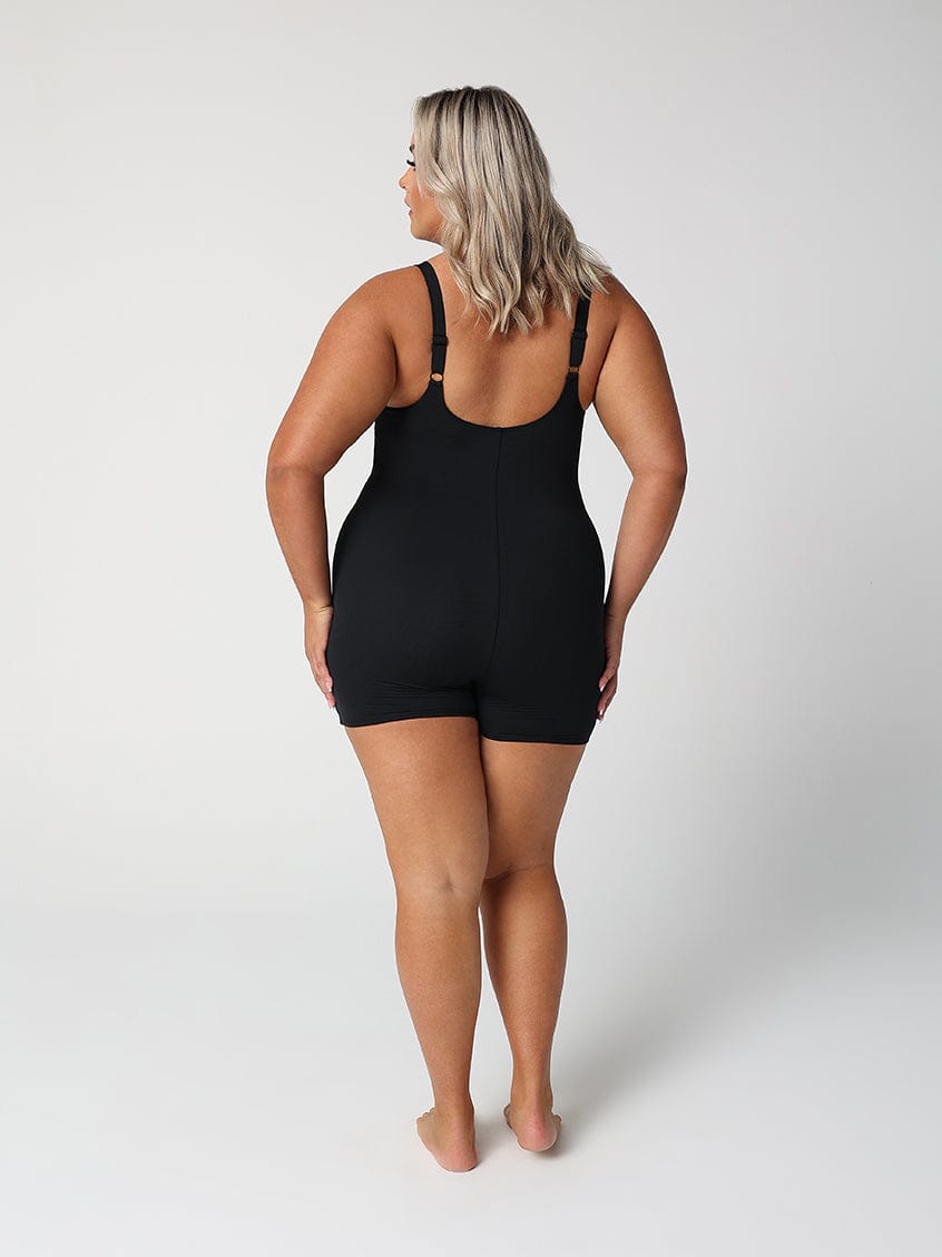 back of lady standing in front of a white wall wearing a black boyleg one piece