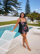 Woman in a floral dress standing by a pool with trees and chairs in the background