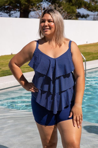 Model standing next to pool wearing plus size navy boy leg swim pant