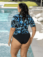 Woman wearing a black and blue floral swim top by a pool