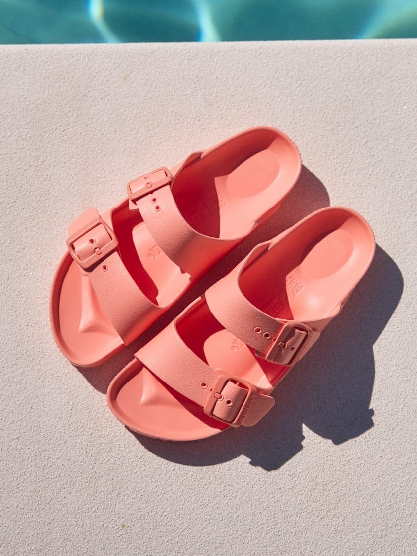 Pair of pink sandals on a light surface with a pool in the background
