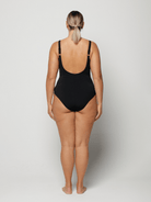 Woman wearing a black criss cross swimsuit with blue floral patterns and scoop back