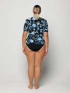 Person wearing a black floral rash guard and black swimsuit bottoms on a white background