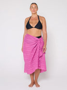 Woman wearing a black bikini and pink sarong on a white background