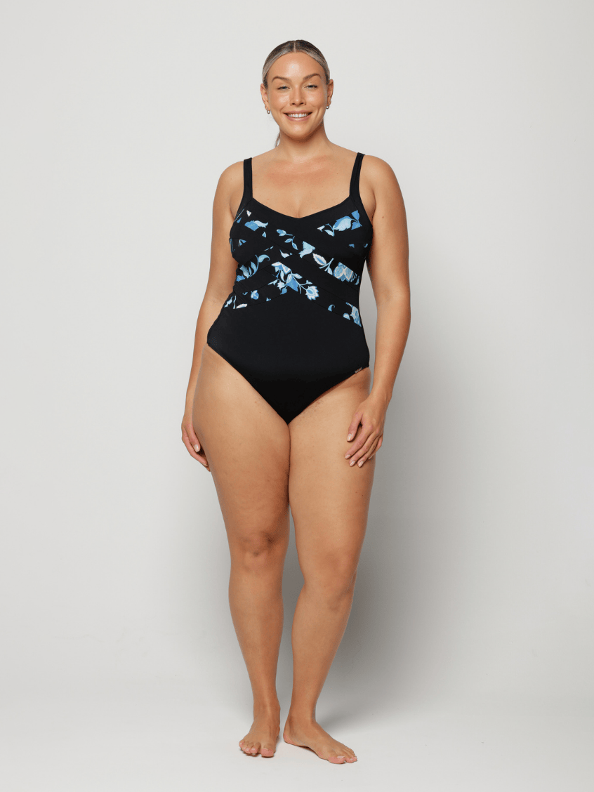 Woman wearing a black criss cross swimsuit with blue floral patterns on a white background