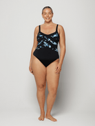Woman wearing a black criss cross swimsuit with blue floral patterns on a white background