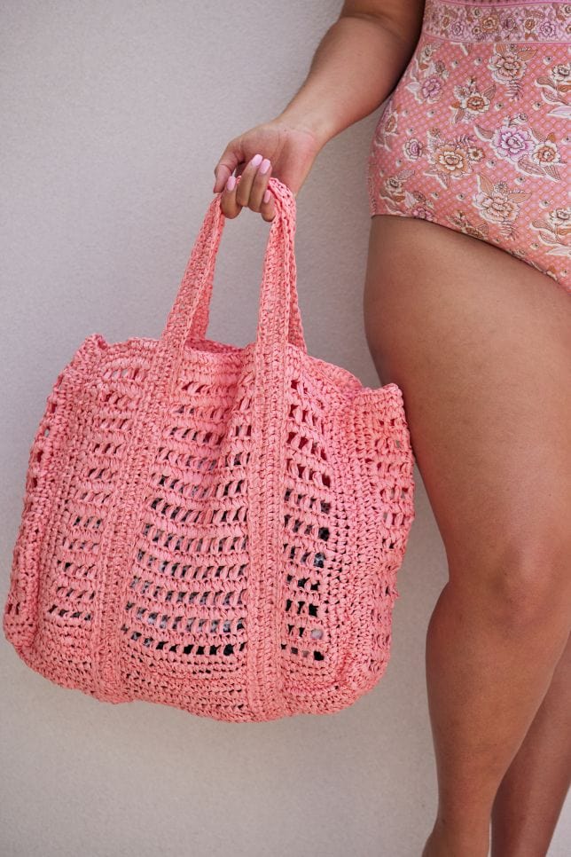 Model holding handmade crochet beach bag in bright peach colour
