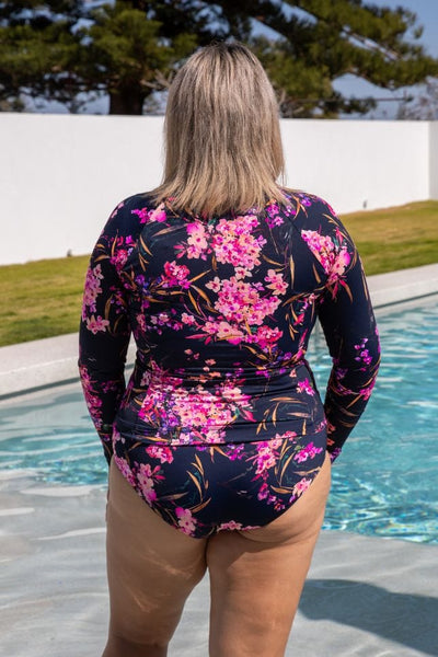 Back of model standing in a pool wearing a plus size flattering long sleeve rash vest with built in shelf bra