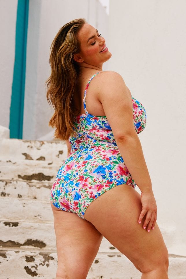 Side of model wearing plus size underwire one piece with ruching detail in bright coloured floral print