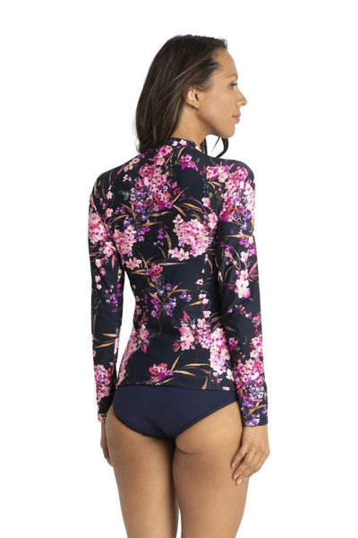 Back of brunette model wearing plus size floral long sleeve rash top in tones of pink and purple 