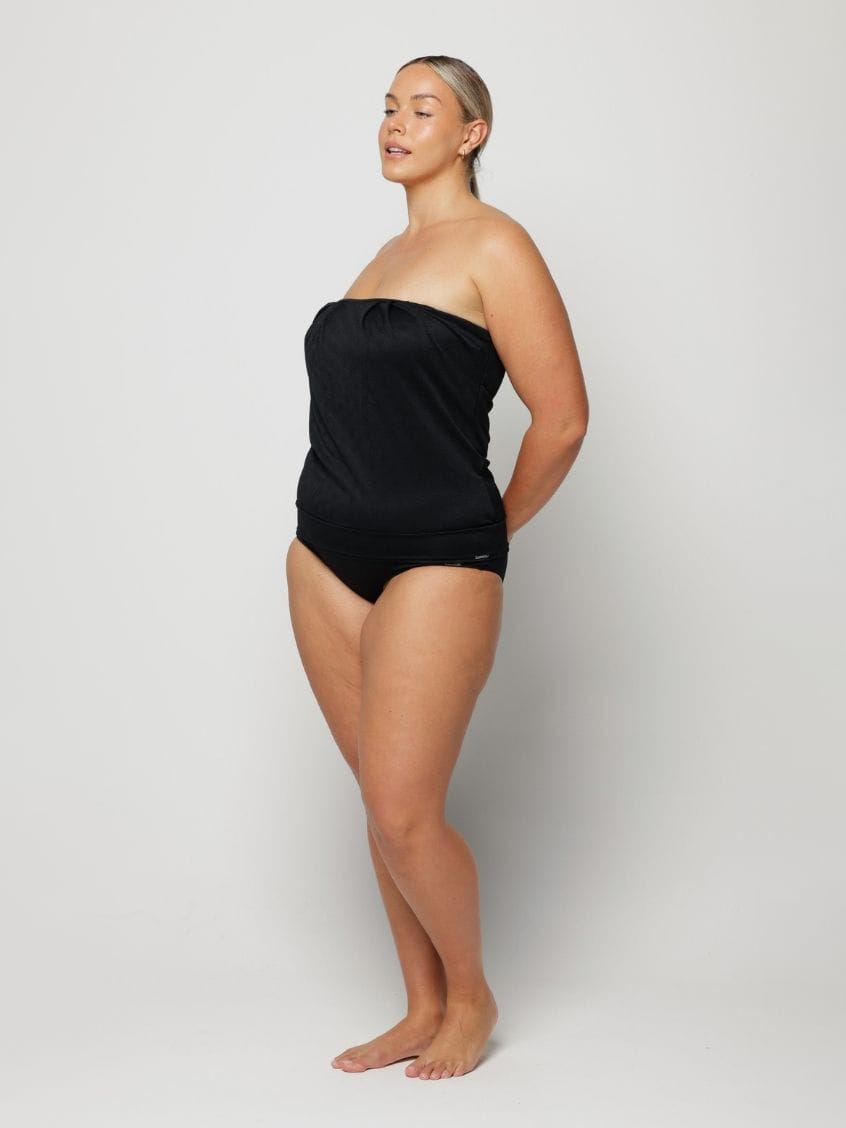Woman wearing a black strapless swimsuit against a white background